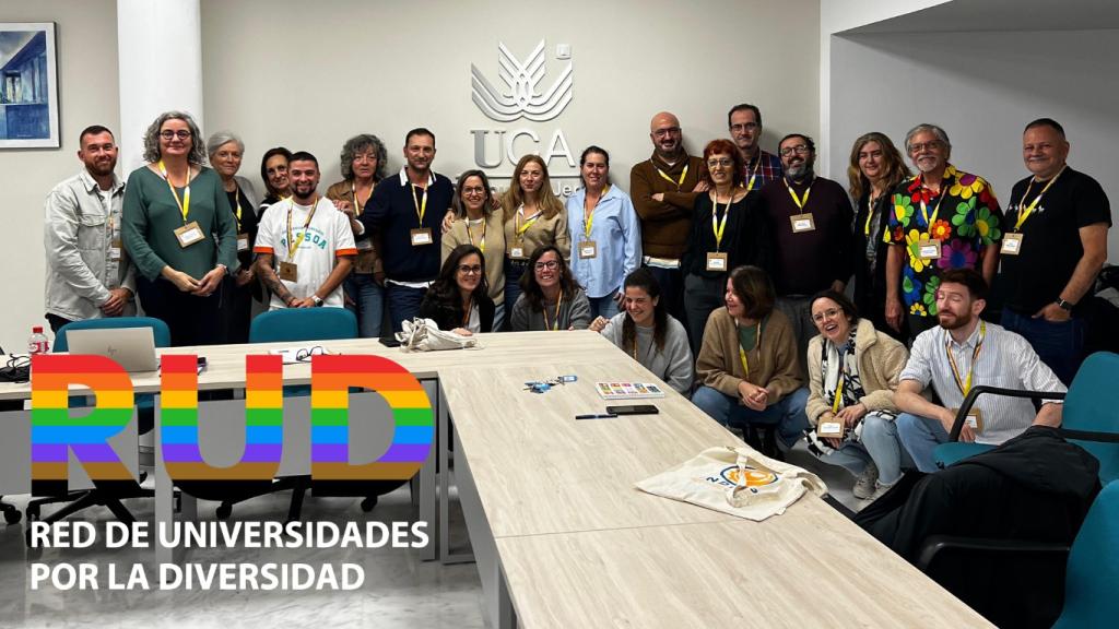 Foto de grupo de todos los participantes del encuentro con su acreditación colgada del cuello, en una sala de reuniones con el logotipo de la Universidad de Cádiz en la pared